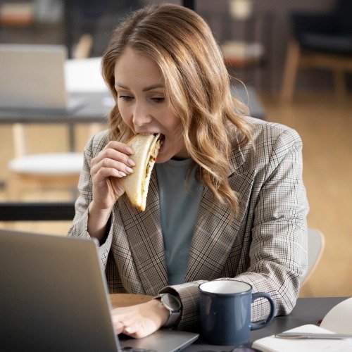 donna che mangia un sandwich davanti al computer al lavoro